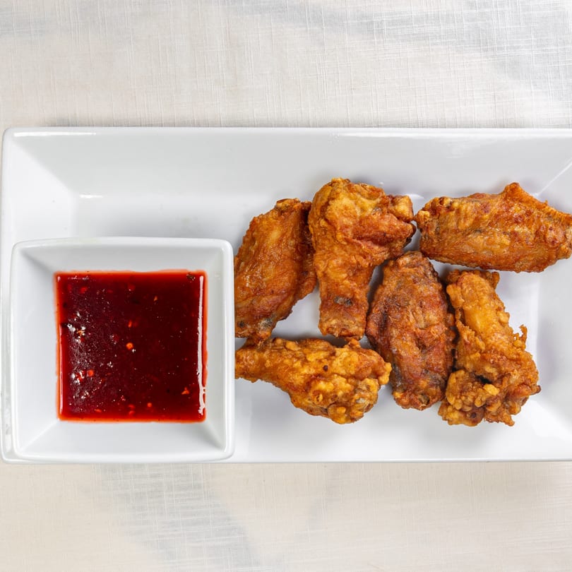 Crispy fried chicken wings with a side of sweet chili dipping sauce on a white rectangular plate.