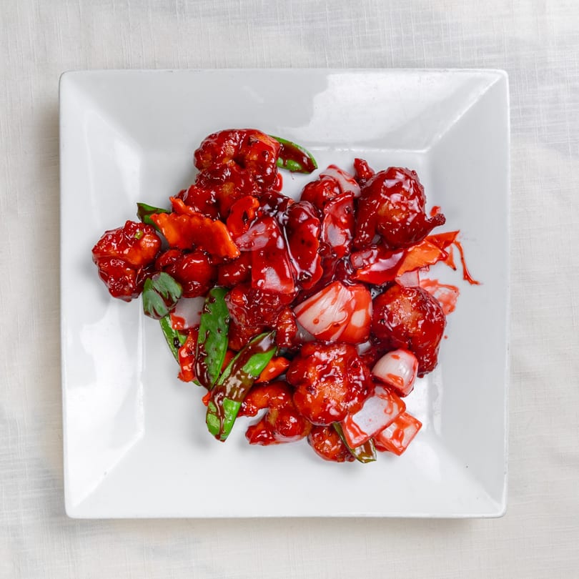 Sweet and sour chicken with red sauce, onions, carrots, and green beans on a white plate.