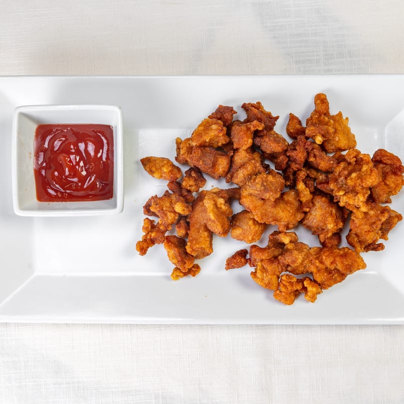 Crispy fried chicken pieces and a small bowl of ketchup on a white rectangular plate.