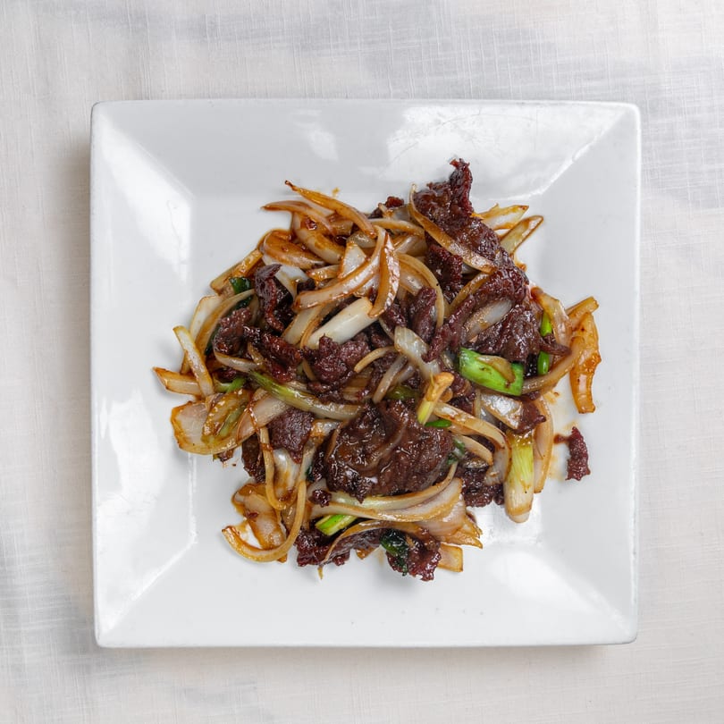 Flaming Wok's Chinese beef and onions stir-fry, glistening with sauce on a white plate.